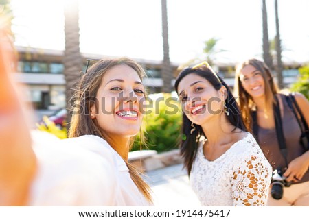 Three happy girls on vacation taking selfies in the city smiling looking at the camera. Beautiful young women having fun with technology and photography outdoor in the city enjoying travel destination