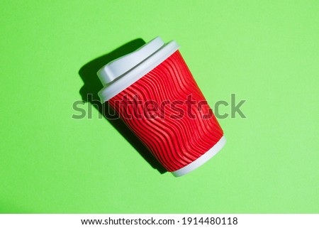 Red paper cup for coffee or tea to go on a green background. Disposable tableware on a colored background with copy space