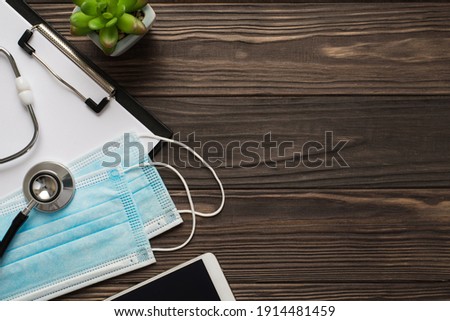 Top flatlay overhead view photo of face masks cell phone plant stethoscope and clipboard on brown dark wooden backdrop