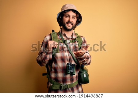 Young hiker man with curly hair and beard hiking wearing backpack and water canteen smiling cheerful offering palm hand giving assistance and acceptance. Royalty-Free Stock Photo #1914496867
