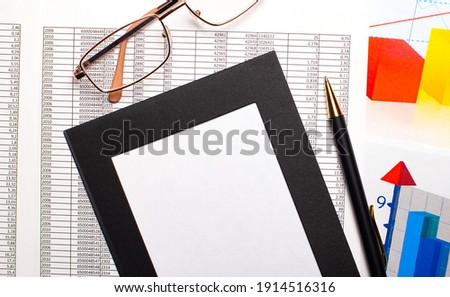 On the desktop are color charts and reports, gold-framed glasses and a blank sheet of white paper in a black frame. Business concept. Top view with copy space