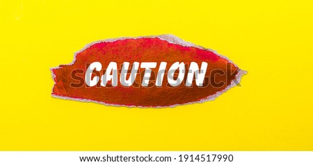 On a yellow background, a sheet of red paper with the word CAUTION