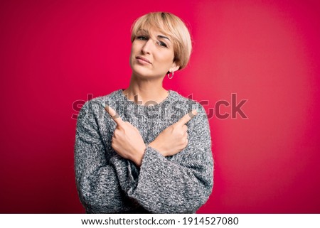 Young blonde woman with modern short hair wearing casual sweater over pink background Pointing to both sides with fingers, different direction disagree