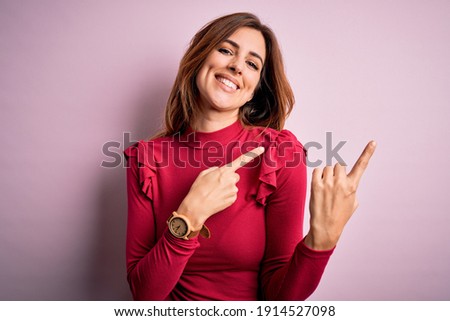 Young beautiful brunette woman wearing casual sweater stnding over pink background smiling and looking at the camera pointing with two hands and fingers to the side.
