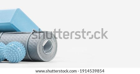 Rolled blue yoga mat and foam block or brick, massage ball. Gender neutral fitness and exercise concept accessories with copy space. Active lifestyle. Workout at home or gym, sports club banner Royalty-Free Stock Photo #1914539854