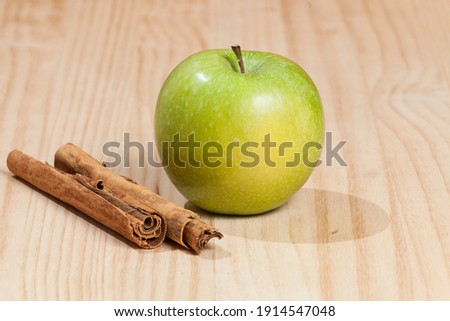 Green apple with a cinnamon stick; photo on wooden background.