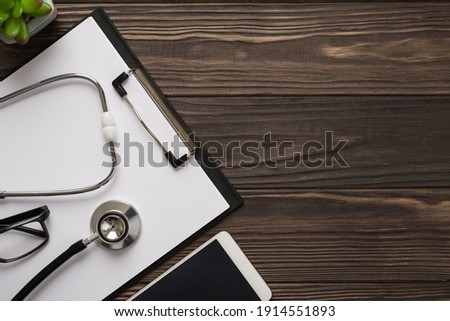 Doctor's workplace concept. Top view photo of clipboard with sheet of paper stethoscope cellphone plant on wooden dark backdrop
