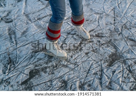 Pair of white leather artistic dancing ice skates with red and grey leg warmers on frozen ice lake with snow and blade marks. ice blades, ice skates, figure skating in wintertime