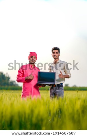 Young indian agronomist or banker showing laptop screen at green wheat field