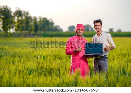 Young indian agronomist or banker showing laptop screen at green wheat field