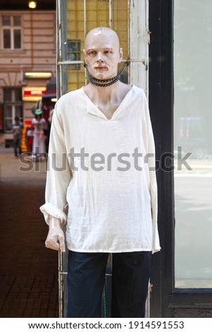 Tied up damaged, aggressive looking one armed male manikin with white shirt on the street; color photo.