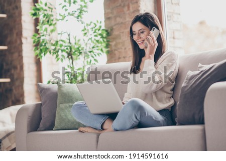 Profile side photo of brown haired woman talk phone listen use laptop wear glasses stay home sit sofa indoors house