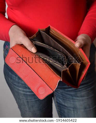 hands of young woman in red blouse and jeans, holding an open empty red purse. Studio shot, close-up.