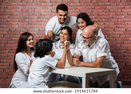 Playful Indian Asian kid and Grandfather Arm wrestling at home with other family members looking, wearing white cloths