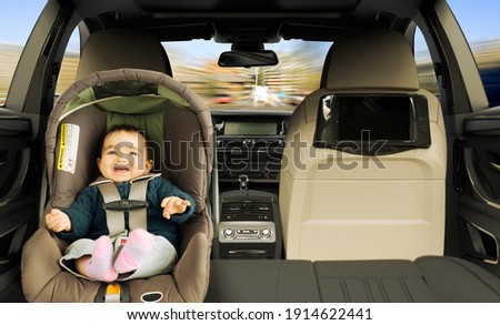 A baby girl in the back seat of a car in a child safety seat.