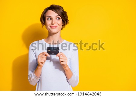 Photo portrait of girl holding credit card looking at blank space isolated on bright yellow colored background