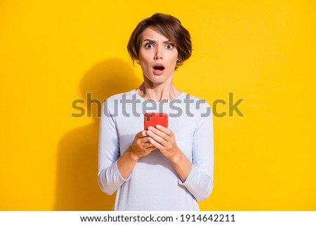 Photo portrait of shocked girl holding phone in two hands isolated on bright yellow colored background