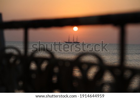 
Sailing ship at sea at sunrise photographed through a wrought iron fence.