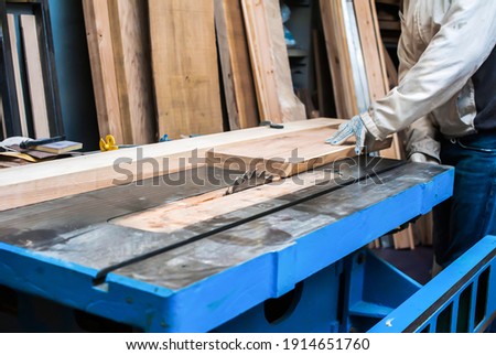 a man cuts a board on a stationary circular saw in a carpentry workshop Royalty-Free Stock Photo #1914651760