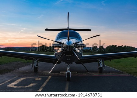 Single turboprop aircraft on evening runway after sunset. A single-engine plane is parked on the runway, bathed in the evening sun. Beautiful color view of the plane. Royalty-Free Stock Photo #1914678751