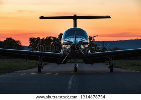Single turboprop aircraft on evening runway after sunset. A single-engine plane is parked on the runway, bathed in the evening sun. Beautiful color view of the plane. Royalty-Free Stock Photo #1914678754