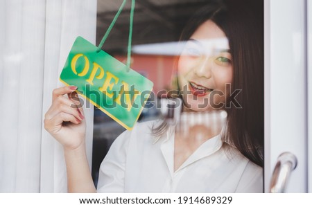 Smiling, young Asian woman and hand turning open sign board on glass door in coffee shop. Lady owner retail, restaurant