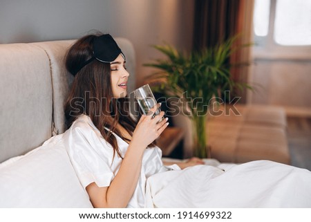young woman drinks water in the bed. model with brown hair with a glass of water in the bed in the bedroom. drink a glass of water in the morning or before bed. young woman enjoying drinking water Royalty-Free Stock Photo #1914699322