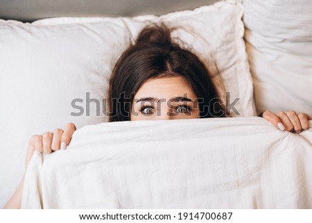 model woman hiding under the blanket. Young woman is very scared. Woman with big open eyes in bed Royalty-Free Stock Photo #1914700687