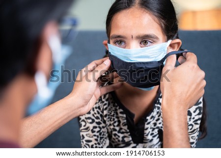 Shoulder shot of father helping his daughter to wear double or two face mask at home to protect from coronavirus covid-19 pandemic before going out
