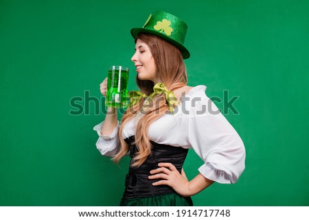 Woman in festive saint patrick's day costume and hat decorated with shamrock holding a mug of green beer, isolated on green background.