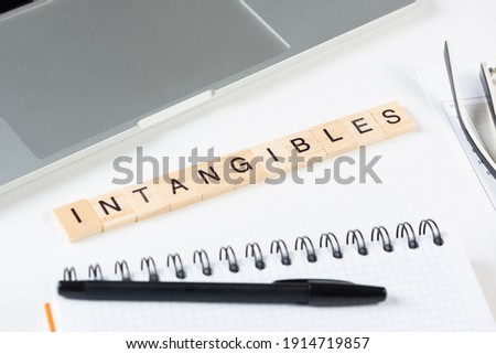 Intangibles concept with letters on wooden cubes. Still life of office workplace with supplies. Flat lay white surface with laptop computer and notepad. Intellectual capital and property. Royalty-Free Stock Photo #1914719857