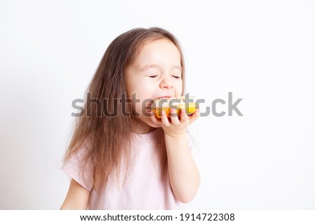 The girl is happy to bite off the doughnut. Fast food. Sweets. Snack. Healthy food. Harmful food. Food habits. Eating children. Emotions. Pleasure. High quality photo