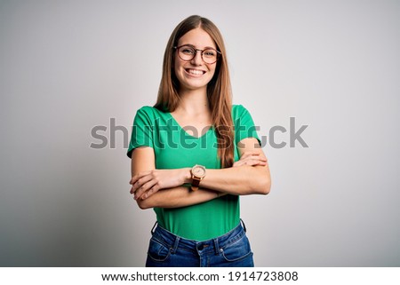 Young beautiful redhead woman wearing casual green t-shirt and glasses over white background happy face smiling with crossed arms looking at the camera. Positive person.