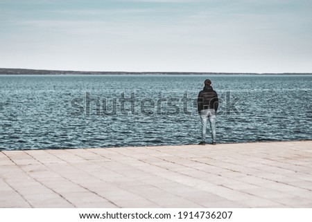 a lonely man stands on the shore of the lake and looks into the distance. View from the back. High quality photo