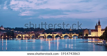 Prague riverside on sunset at twilight. Panoramic image of illuminated Charles Bridge and Novotnevo Lavka riverside buildings with a clock tower