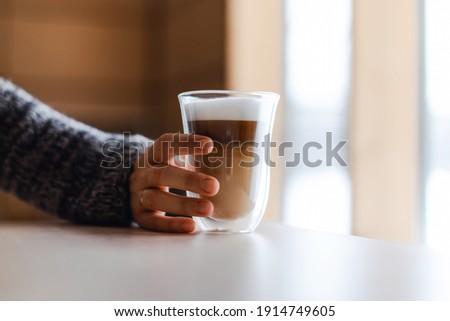 Woman's hand in gray sweater puts milk foam in cappuccino.