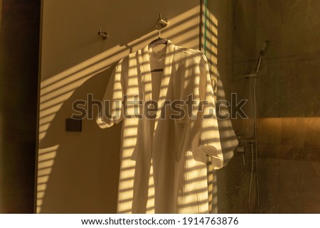 The bathrobes were hung in the shower area and there was light that passed through the blinds.