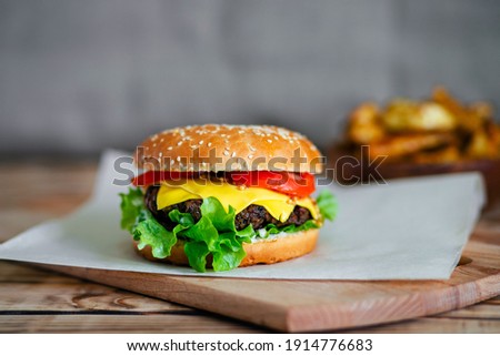 A delicious homemade cheeseburger with French mustard sits on the chopping board. On the background, the potato slices are blurred