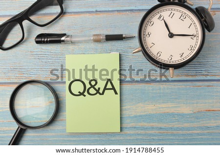 Top view of a magnifying glass, pen, alarm clock and spectacles with written Q and A on wooden background. Selective focus.