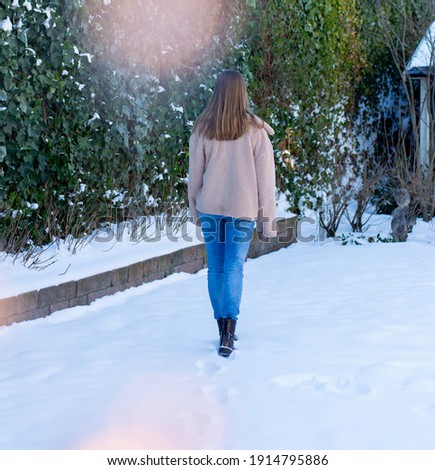 A Caucasian teenage girl walking in the snow with her furry light brown coat on. There are blurry fairy lights in the front to give it a festive look. Outdoors photo of a child in the white snow. 