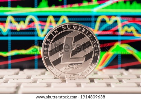 Close up photo of silver shining lite coin standing on white button of keyboard with multicolored digital diagrams on the screen display monitor on the background