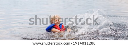 Funny girl in lifeguard jacket swimming in lake. Child kid splashing in water river. Authentic candid lifestyle happy childhood. Summer fun outdoor aquatic activity. Web banner header.