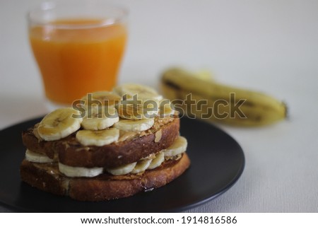 Peanut butter banana honey toast sandwich served with Orange juice, an easy breakfast idea. Shot on white background.
