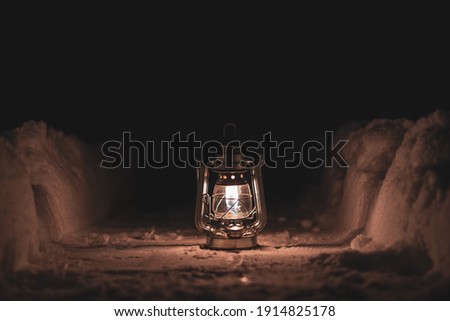 a burning oil lamp stands on a snowy path at night