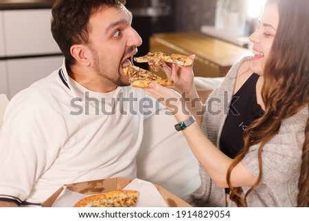 Girl feeds her husband with two slices of pizza. Exaggerate and wondering. Much credit on yourself and capabilities concept. Royalty-Free Stock Photo #1914829054