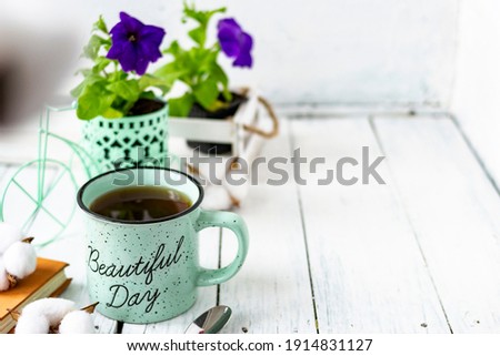 Close-up of a cup of tea on a wooden white table with blurred background, front blur. Still life with flower, book, teaspoon, cotton box. Spring breakfast. Copy space