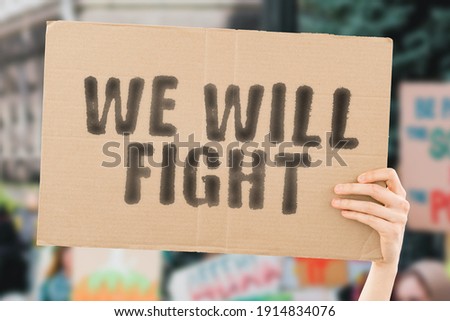 The phrase " We will fight " on a banner in men's hand with blurred background. Protest. Motivation. Rally. Future. Fighting. Rally. Serious. Process. Protester. Activist. Pandemic. Resistance Royalty-Free Stock Photo #1914834076