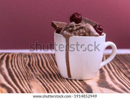 pudding with ice cream, cherries and pieces of chocolate in a mug on a jjon wood table. Melted ice cream flows in a mug on a pink background. High quality photo