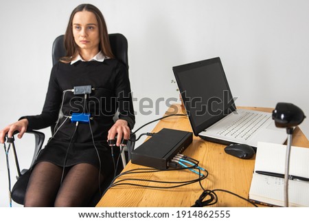 Concentrated, thoughtful, pretty girl, is in a bright room, polygraph testing. The girl is wearing sensors for the passage of the polygraph, sitting in a chair. The concept of truth, polygraph