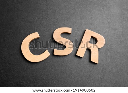 Wooden letters CSR on black background, flat lay. Corporate social responsibility concept